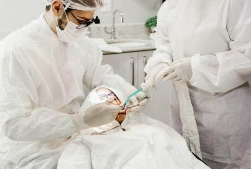 Two dentists in protective gear performing a procedure on a patient in a clinic